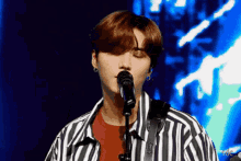 a young man in a striped shirt is singing into a microphone on a stage .