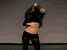 a woman in a black crop top and leather pants is dancing in a room .