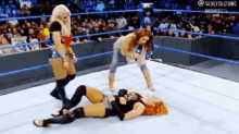 a woman is laying on the ground in a wrestling ring while two other women stand around her