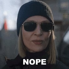 a woman wearing sunglasses and a beanie has the word nope written on her face