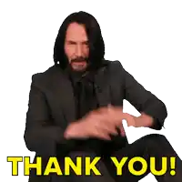 a man in a suit and tie is sitting down and giving a thank you gesture