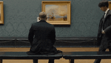 a man sits on a bench in front of a painting