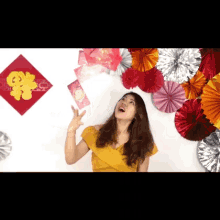 a woman in a yellow top is throwing red envelopes in the air with chinese writing on them