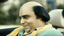 a bald man is sitting in the back seat of a car and smiling .