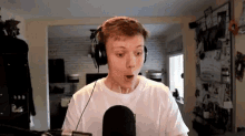 a man wearing headphones and a white shirt is standing in front of a microphone