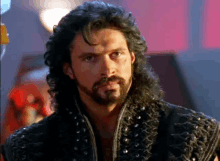 a man with curly hair and a beard is wearing a black vest with studs