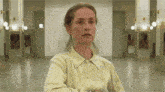 a woman in a yellow shirt is sitting in a hallway with a serious look on her face .