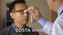 a man wearing glasses is getting his eyes examined by a doctor and says `` costa who '' .