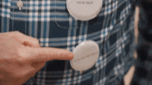 a person is pointing at a button on a blue plaid shirt .