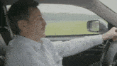a man in a white shirt is driving a car with his mouth open