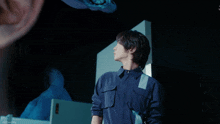 a man in a blue shirt stands in front of a mirror with a reflection of a person 's ear