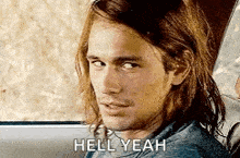 a man with long hair is sitting in the back seat of a car and says `` hell yeah '' .