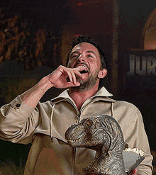 a man holding a statue of a dinosaur in front of a sign that says jura