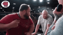 a man in a red shirt is pointing at another man in a grey shirt with the mma logo on the bottom
