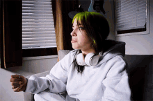 a woman with green hair is wearing headphones while sitting in front of a window