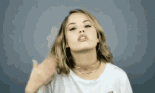 a woman in a white t-shirt and choker is blowing a kiss at the camera .