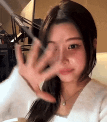 a woman covering her face with her hand while wearing a white sweater