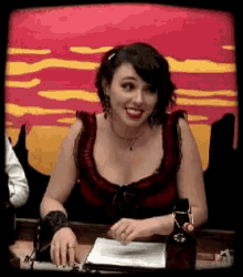 a woman in a red top is smiling while sitting at a table with a bottle of wine