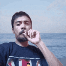 a man with a beard wearing a greenlight shirt smoking a cigarette