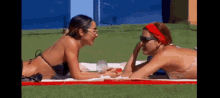 two women in bikinis are laying on a red and white towel
