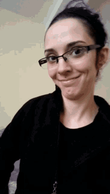 a woman wearing glasses and a black jacket smiles at the camera