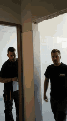 two men standing in a doorway one of whom is wearing a shirt which says ' dimmag ' on the back