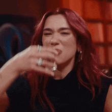 a woman with red hair is drinking from a glass while sitting at a table .