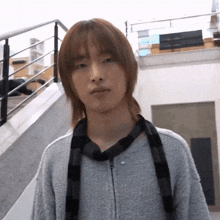 a young man with long hair and a scarf around his neck is standing in front of stairs .