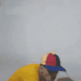 a man wearing a yellow shirt and a red green and white hat is throwing a baseball