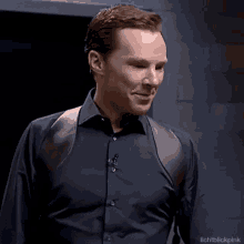 a man wearing a black shirt with a leather shoulder strap is standing in a dark room .
