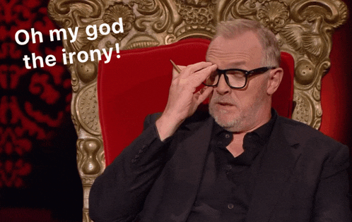 a man in a suit and glasses is sitting in a chair with the words oh my god the irony written above him