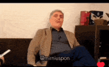 a man in a suit is sitting on a couch with the name mirniuspon written on the bottom