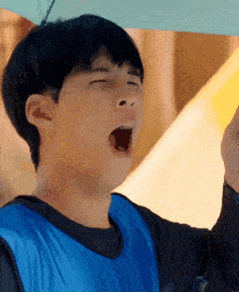 a man in a blue vest is yawning with his mouth open