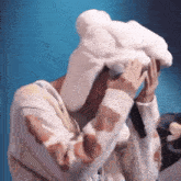 a person wearing a cow print sweater and a white hat is covering their face with their hands .