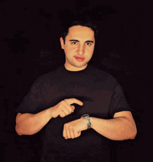 a man in a black shirt is pointing at his wrist watch
