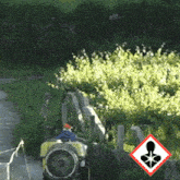 a man is driving a sprayer down a path with a warning sign behind him