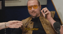 a man wearing sunglasses and a leather vest is talking into a microphone and says " fait peter "