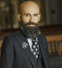 a bald man with a beard is wearing a black suit and tie .