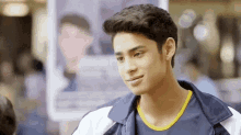 a young man is smiling in front of a picture of a man in a blue shirt .