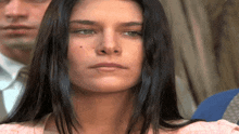 a woman with long dark hair looks at the camera with a man in a suit behind her