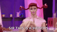 a drag queen with pigtails is making a heart with her hands .
