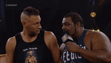 a man wearing a tank top that says ' eedil ' on it talks into a microphone