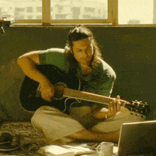 a man sitting on the floor playing an acoustic guitar
