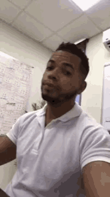 a man in a white polo shirt is taking a selfie in a room .