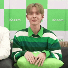 a man in a green and white striped shirt is sitting on a couch with a green pillow