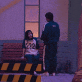 a girl wearing a 222 shirt sits on a bench next to a man