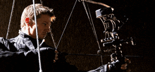 a man in a black jacket is holding a bow and arrow in his hands