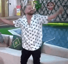 a man in a polka dot shirt is standing in front of a pool with his arms outstretched .