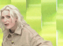 a woman with blonde hair is standing in front of a green wall .