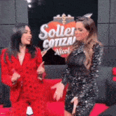 two women standing next to each other in front of a sign that says solter cotiza nicol